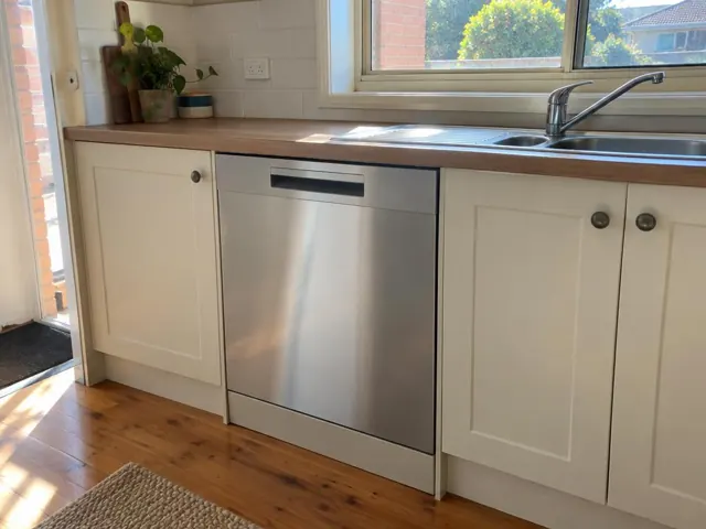 Integrated dishwasher beneath a timber benchtop beside a stainless sink in a cream kitchen in West Wallsend