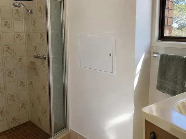 Neat access panel on a painted bathroom wall beside a shower and window in Cameron Park