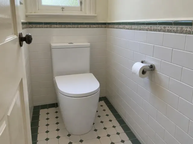 White toilet in a tiled small bathroom with patterned floor and wall trim in Wallsend